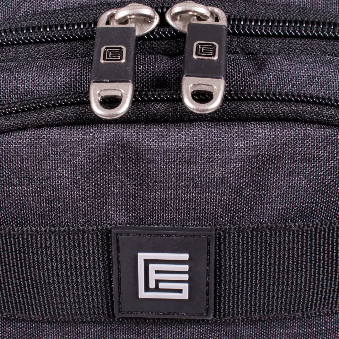 Close-up of a dark gray textured fabric bag with dual silver zipper pulls and a black rectangular logo patch featuring a white stylized 'E' on a webbing strap.