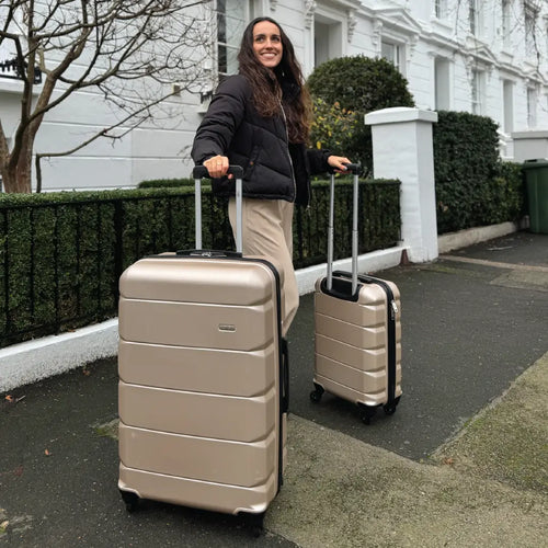 Person holding two gold suitcases on a street with a building in the background
