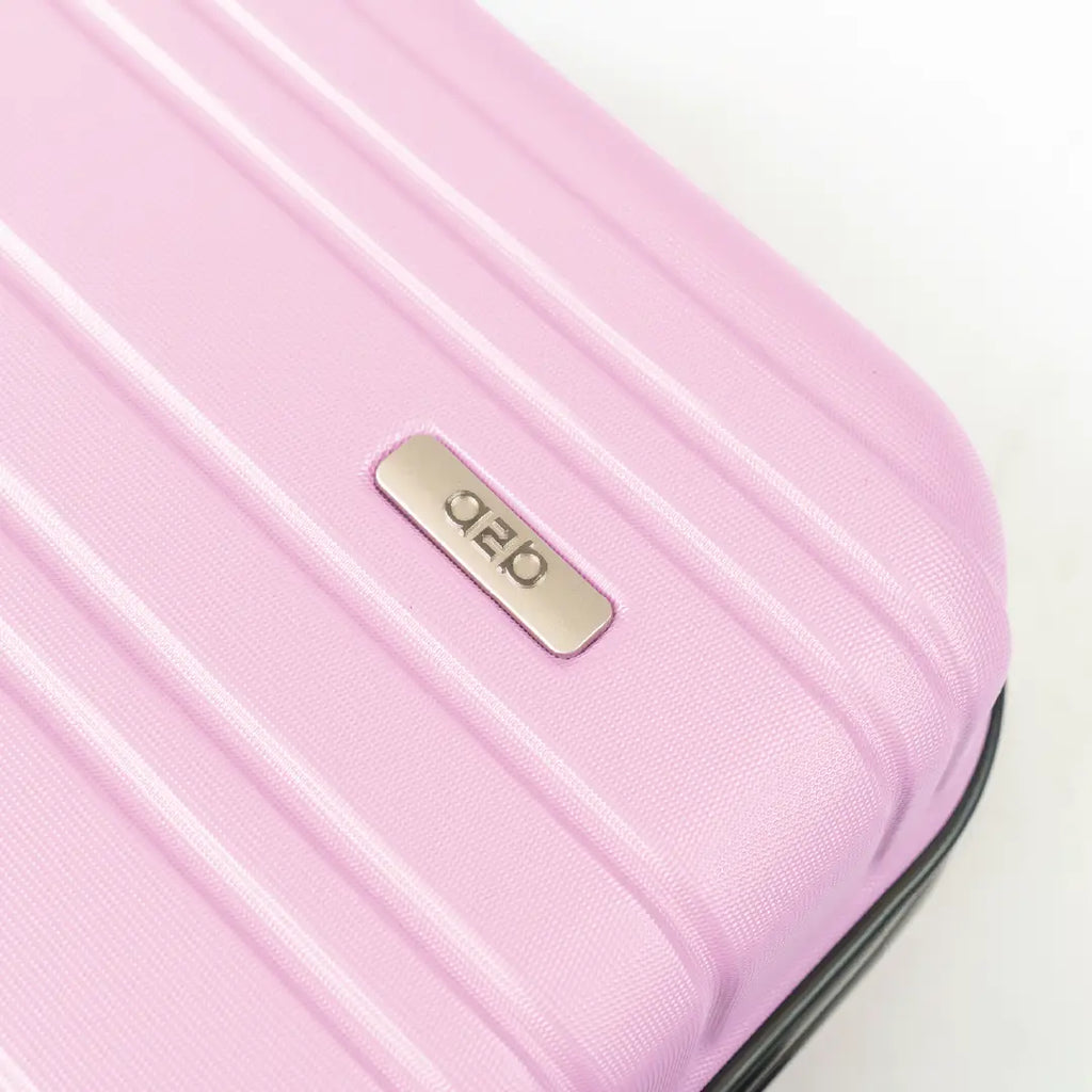 Close-up of a pink suitcase with a gold brand logo on a light background