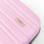 Close-up of a pink suitcase with a gold brand logo on a light background