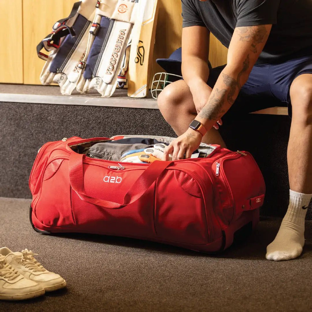 Person packing a red duffel bag with sports equipment in a room.