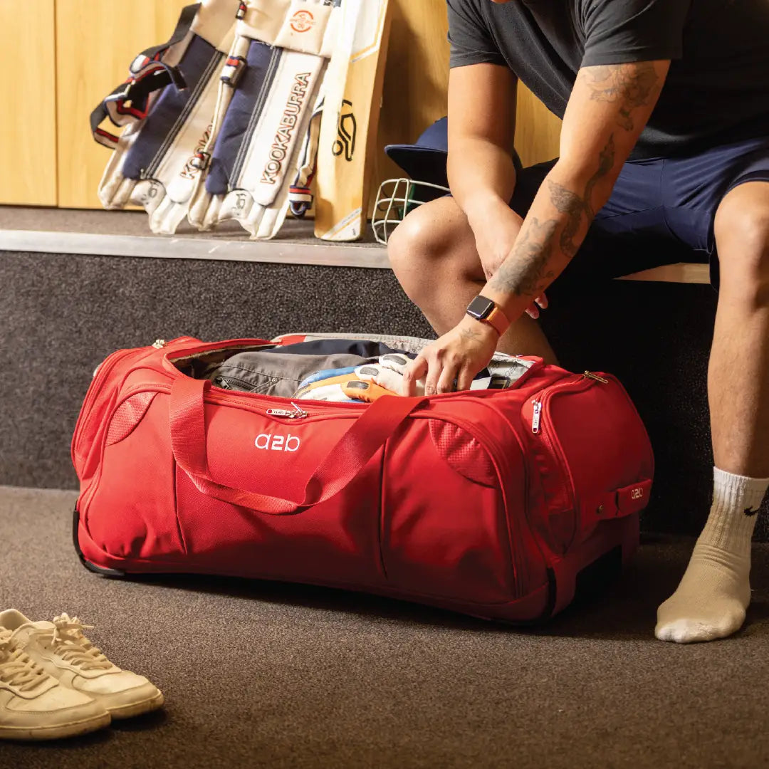 Person packing a red duffel bag with sports equipment in a room.