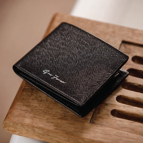 Black textured wallet with branding on a wooden surface