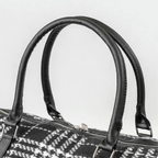 Close-up of a black and white patterned handbag with handles on a light gray background