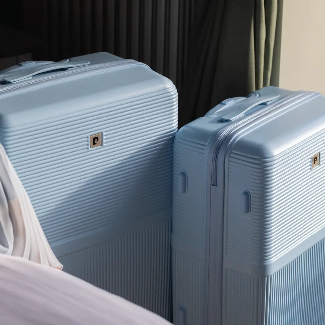 Two light blue suitcases with a visible brand logo on a bed.