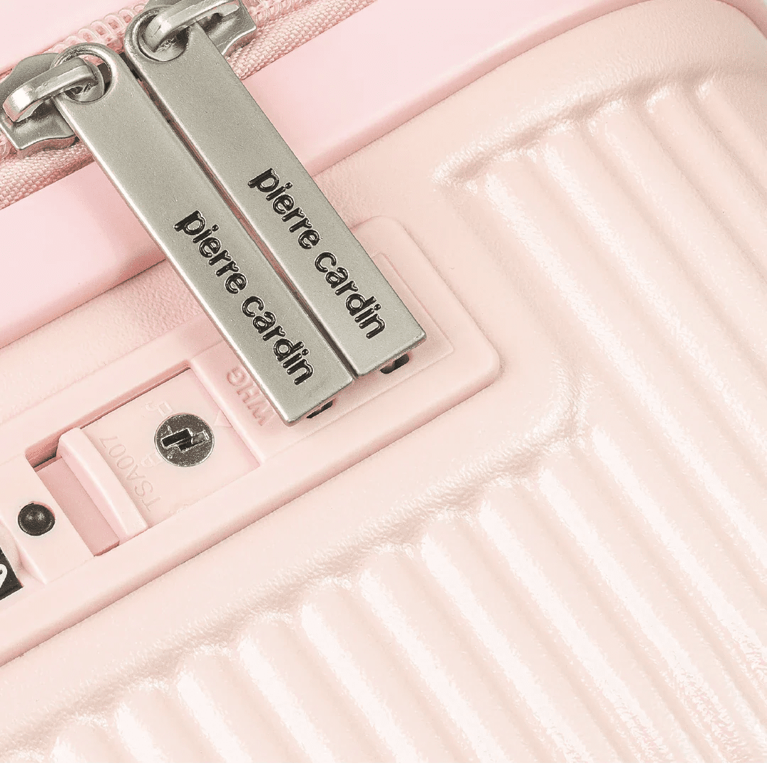 Close-up of a pink suitcase with 'Pierre Cardin' branding on a metallic tag.