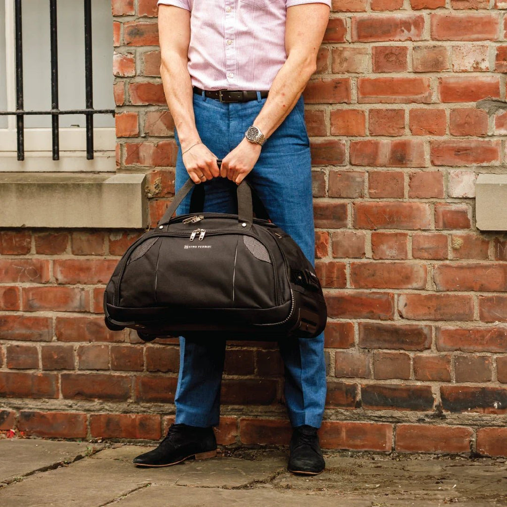 Person holding a black duffel bag against a brick wall
