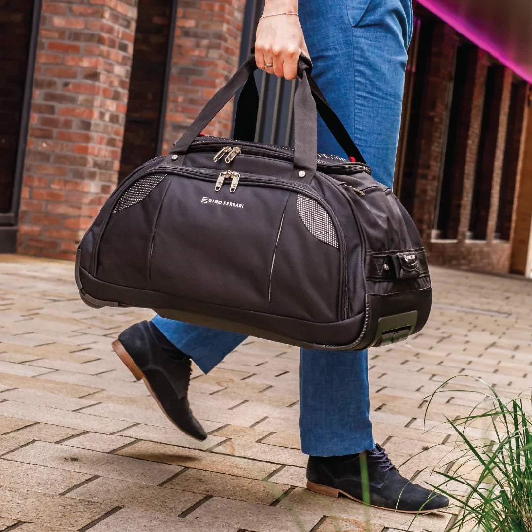 Person holding a black duffel bag with branding on a brick pavement.