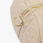 A close-up of a beige bag with patterned stitching and a gold zip.