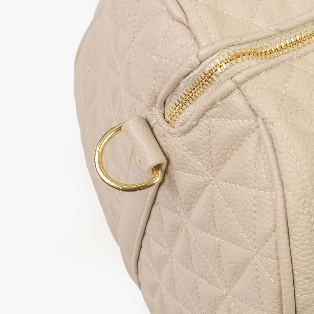 A close-up of a beige bag with patterned stitching and a gold zip.