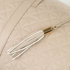 Close-up of a beige bag with patterned stitching and a tassel with gold accents.