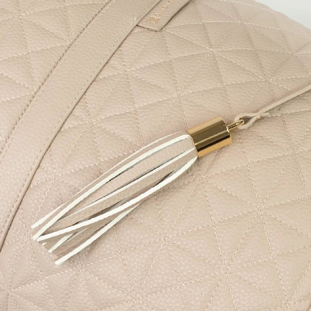 Close-up of a beige bag with patterned stitching and a tassel with gold accents.