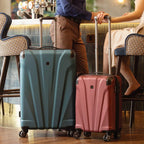Two suitcases, one blue and one pink, on a wooden floor with people in the background.