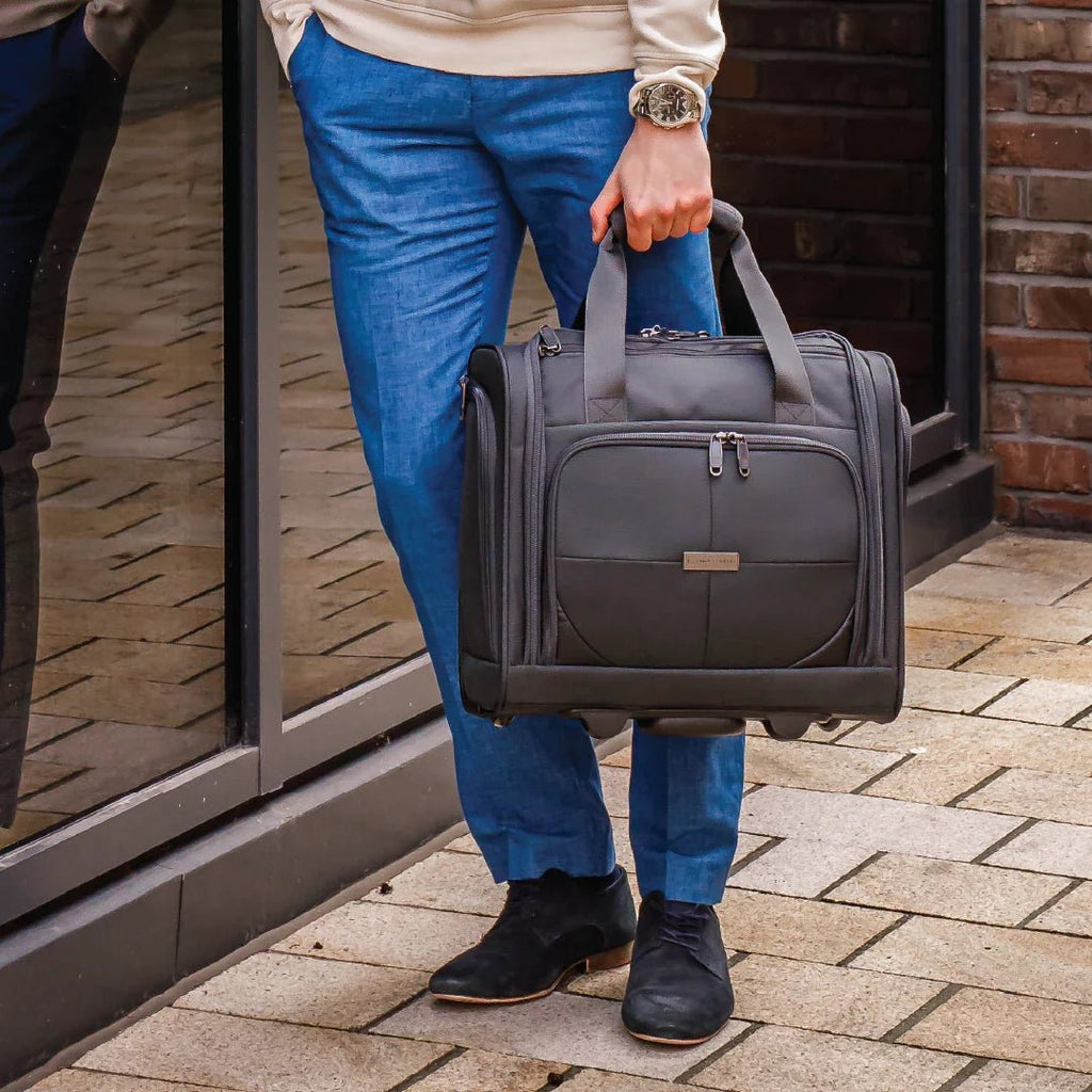 Person holding a gray suitcase on a brick pavement