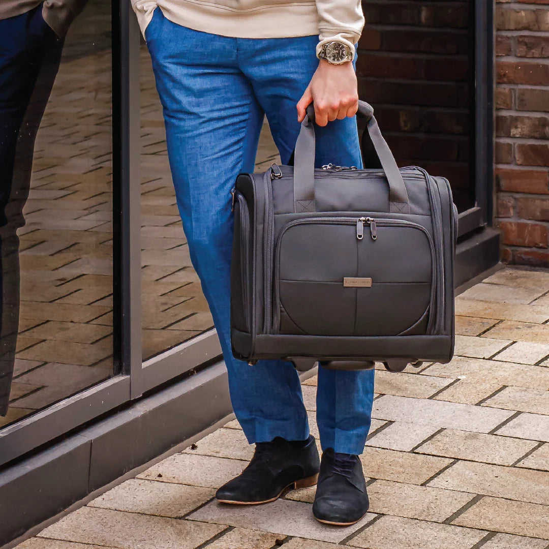 Person holding a gray suitcase on a brick pavement