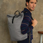 Man wearing a gray backpack against a textured wall.