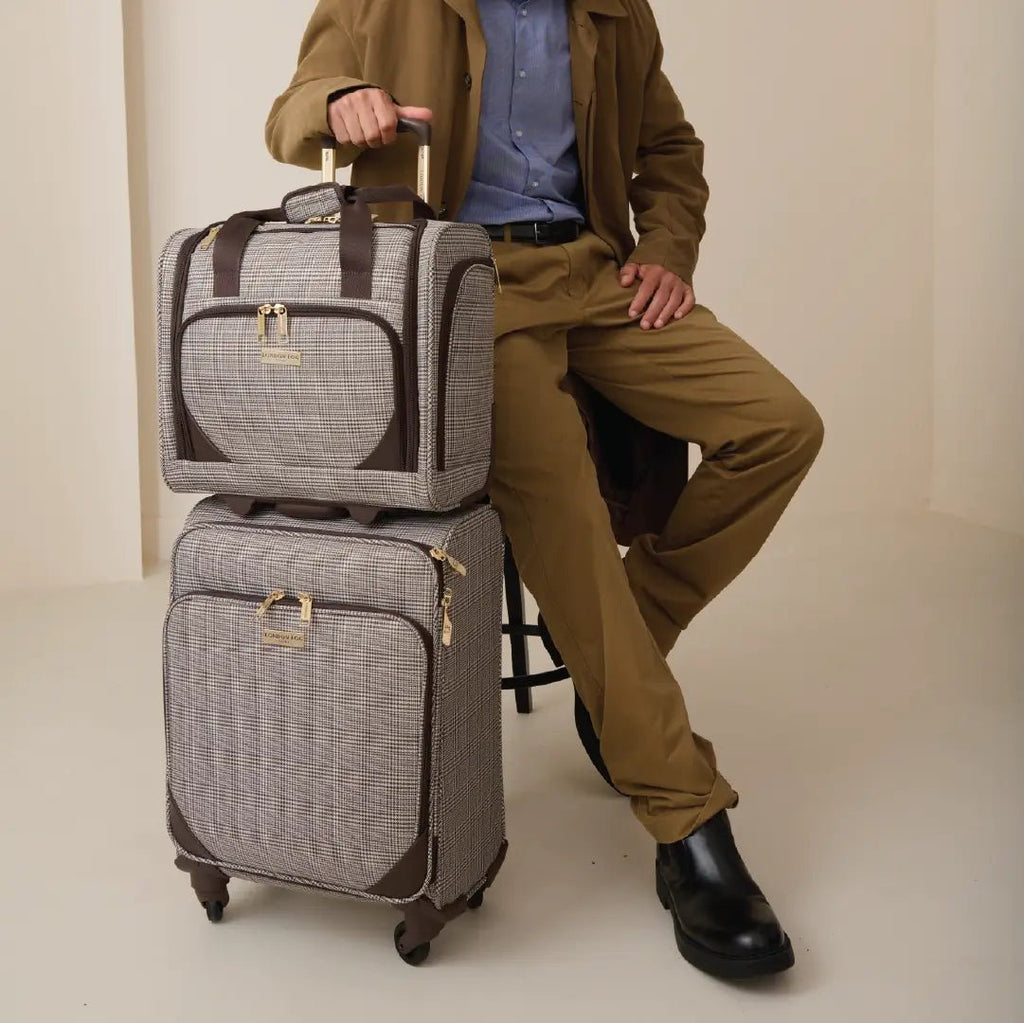 Person holding a stack of gray suitcases with brown accents on a beige background