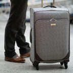 Gray checkered suitcase with wheels on a pavement, person partially visible