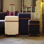 Three suitcases of different colors on a stone floor with a decorative wall in the background.