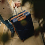 Person holding a blue suitcase with a brown handle on a tiled floor.