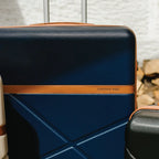 Blue suitcase with brown strap and 'London Fog' branding on a textured wall background
