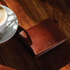 Brown leather wallet on a wooden table with a cup of coffee in the background